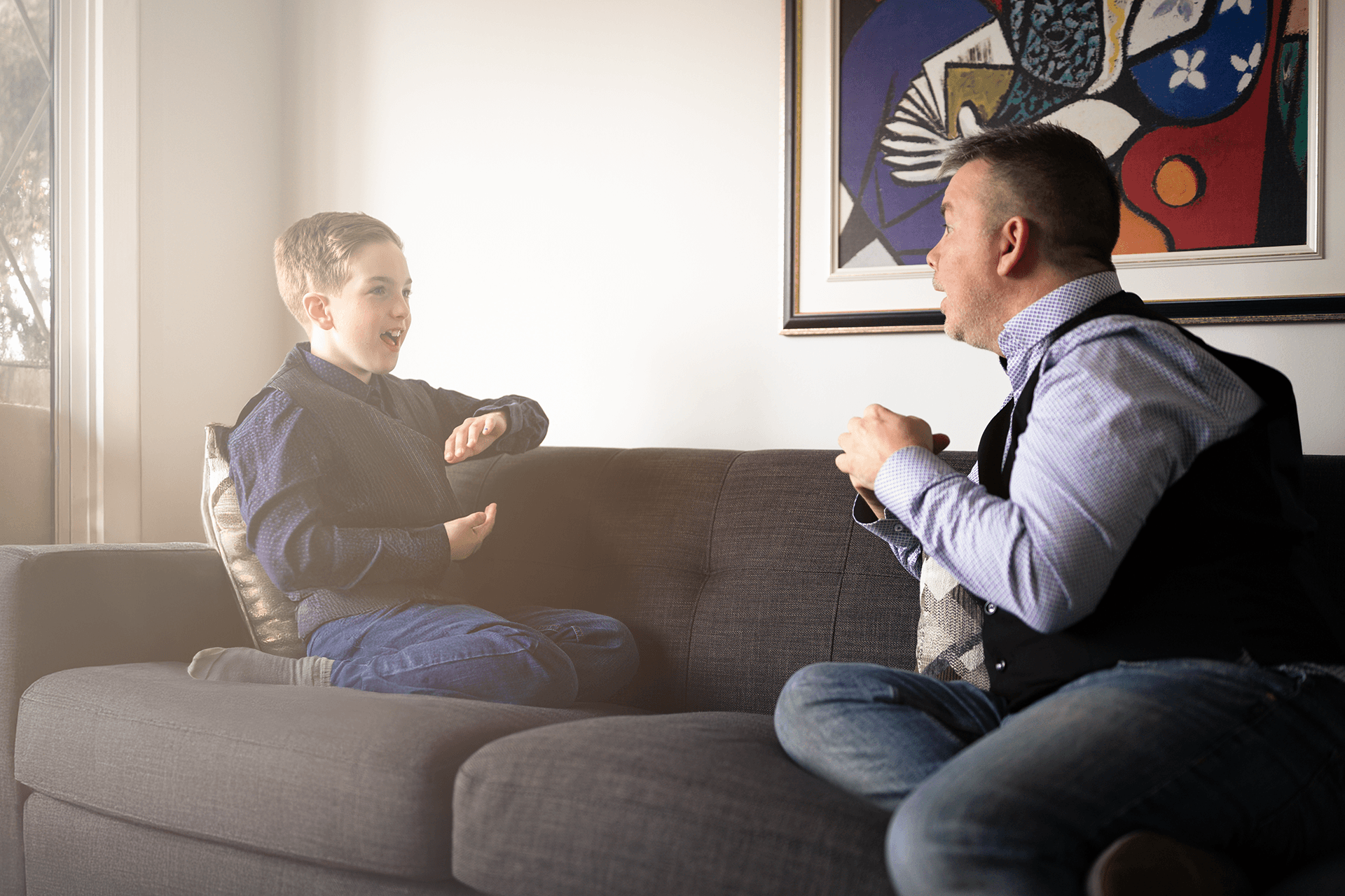 Romain et son père vus de profil, en train de discuter en langue des signes sur un canapé.